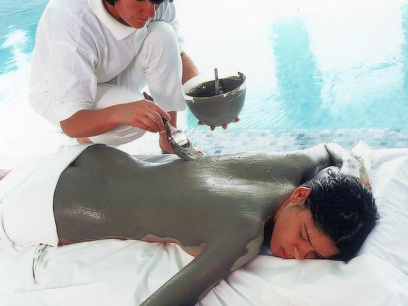 Una donna riceve un trattamento completo di fango accanto a una piscina in una spa.