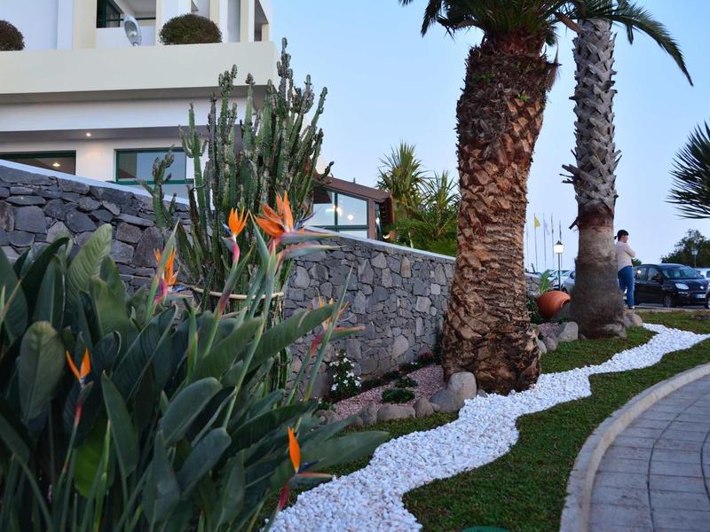 Sentiero con ghiaia bianca tra palme e piante vicino a un complesso alberghiero.