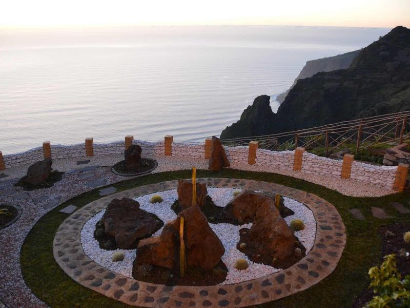 Giardino roccioso con sculture in pietra che si affacciano sul mare e sulle scogliere al tramonto.