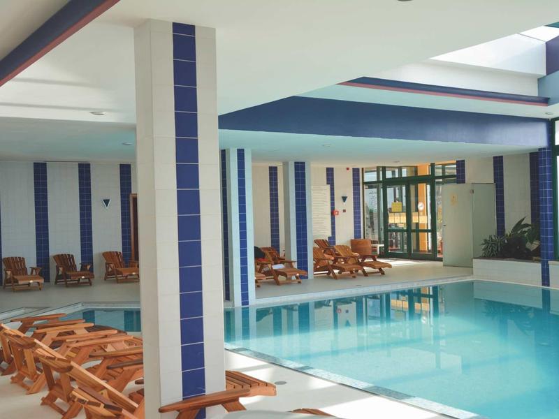 Piscina indoor con piastrelle blu e lettini in legno in un hotel moderno.