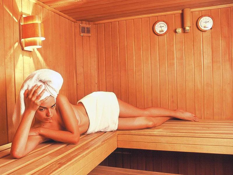 Donna in asciugamano bianco rilassata sdraiata in sauna in legno con termometri.