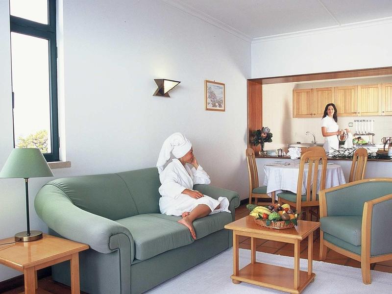 Donna in accappatoio seduta sul divano mentre un'altra donna è in cucina.