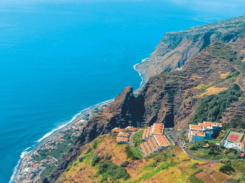 Paesaggio costiero con scogliere ripide, mare blu e villaggi su terreno collinare.