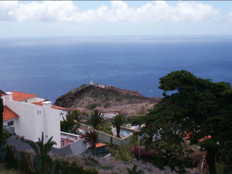 View of the sea from a hillside with white houses and trees in the foreground.