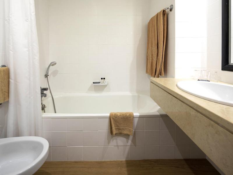 White tiled bathroom with bathtub, towels, and a sink next to a large mirror.