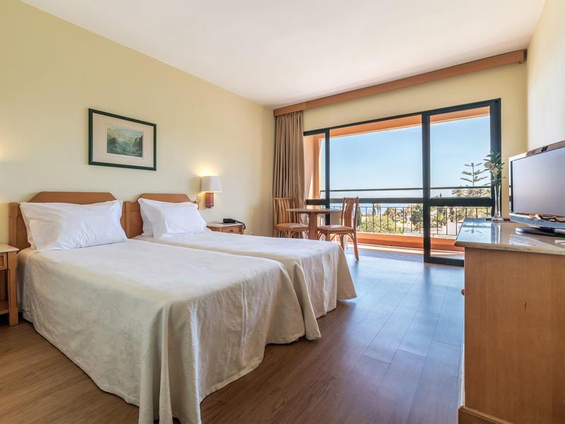 Bright hotel room with two single beds, balcony, and sea view.