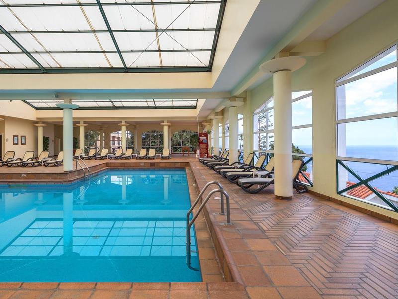 Indoor pool with lounge area and large windows overlooking the sea in a hotel.