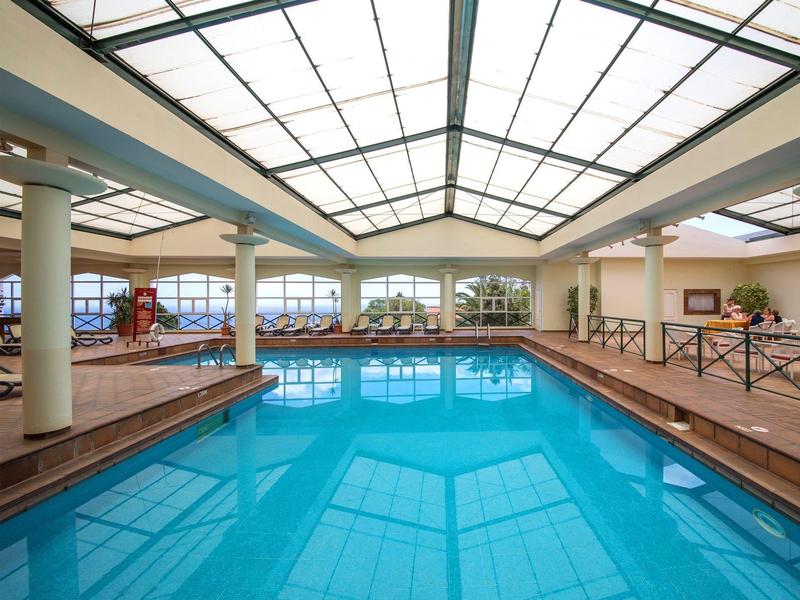 Bright indoor pool with large glass ceiling windows and relaxing lounge areas.