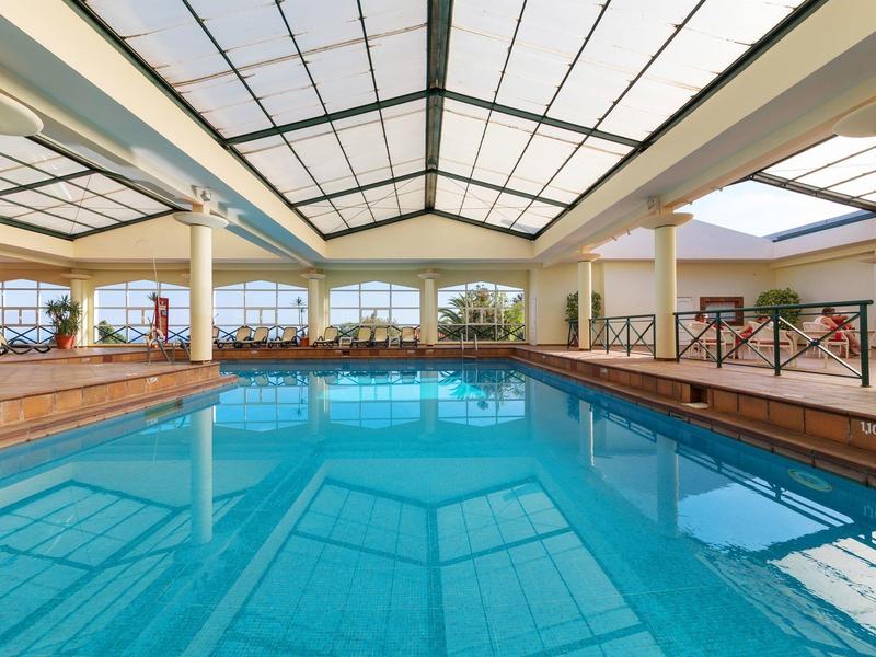 Bright indoor pool with glass roof and seating area in hotel