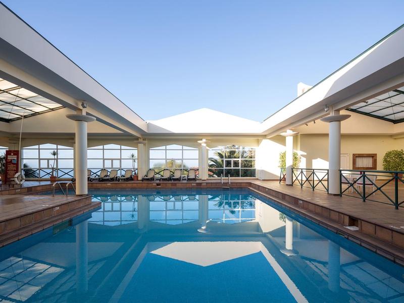 Modern hotel with large indoor pool and lounge chairs under glass roof