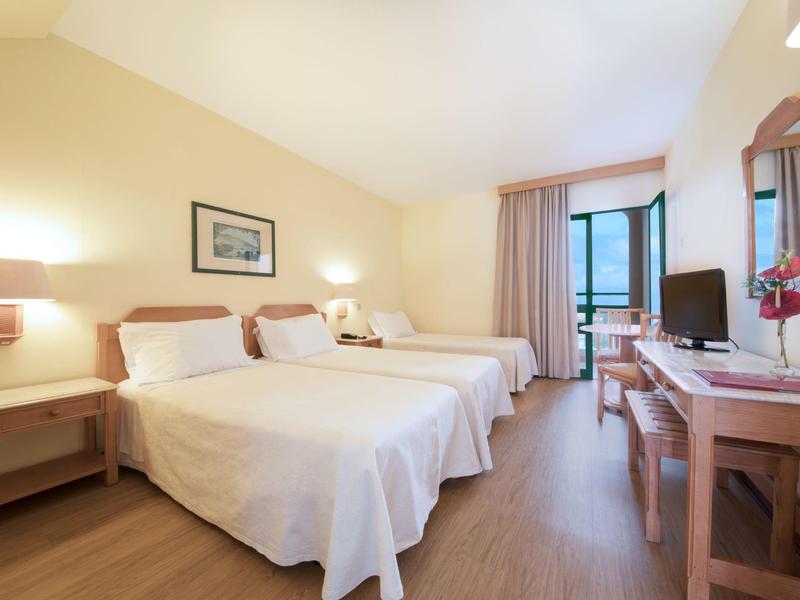 Bright hotel room with two beds, desk, TV, and balcony view.