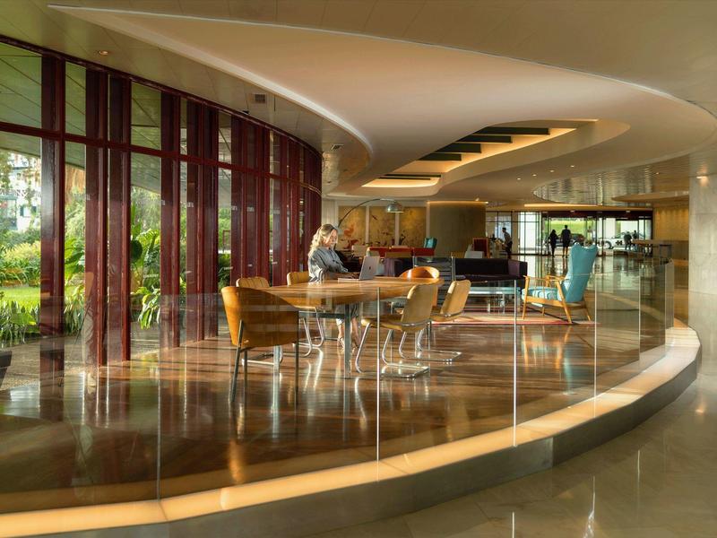 Modernes Café mit großen Fenstern, runden Tischen und gemusterten Stühlen in hellem Ambiente.