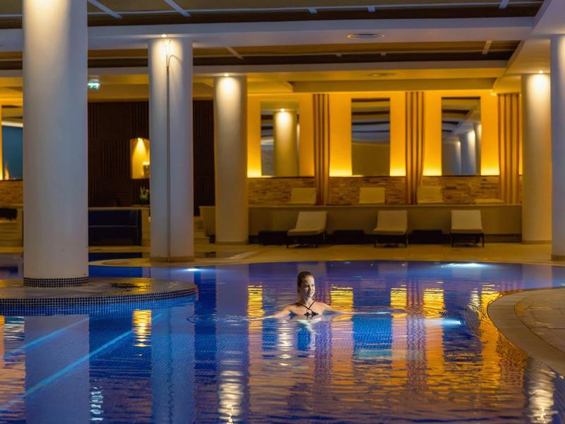 Innenpool mit Säulen, warmem Licht und einer Person im Wasser in entspannter Atmosphäre.