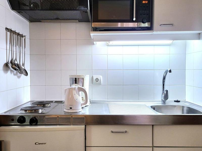 Mała nowoczesna kuchnia z kuchenką, mikrofalówką, zlewem i białą lodówką.