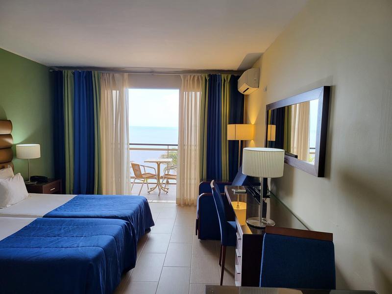 Pokój hotelowy z dwoma łóżkami, biurkiem, krzesłem i balkonem z widokiem na morze.