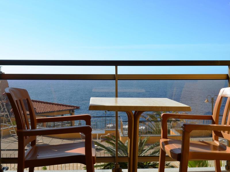 Dwa drewniane krzesła i stolik na balkonie z widokiem na morze w słoneczny dzień.