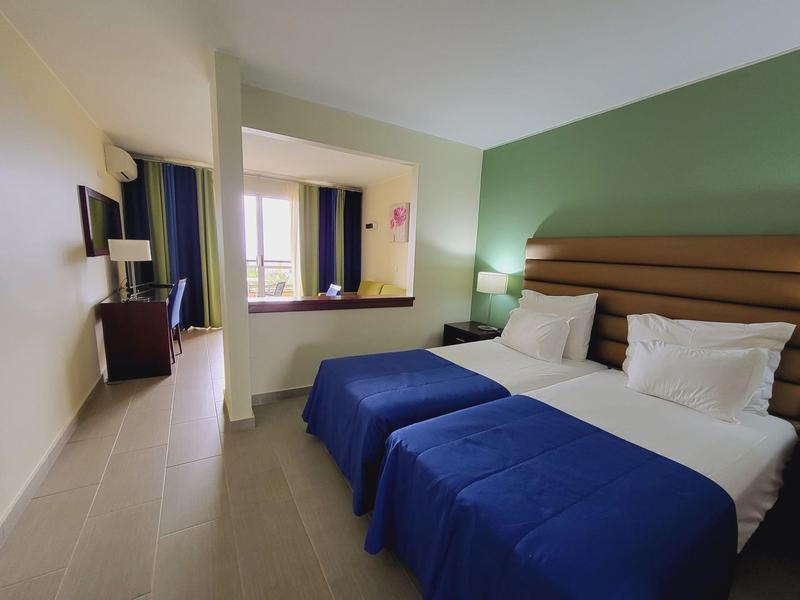 Nowoczesny pokój hotelowy z podwójnym łóżkiem, niebieską pościelą i telewizorem na ścianie.