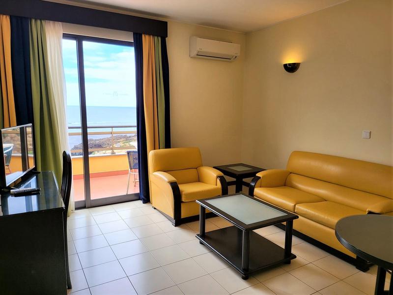 Przytulny salon z żółtą sofą i fotelem, widok na balkon z widokiem na morze.