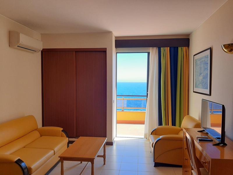 Pokój z dwiema sofami, stołem, telewizorem i widokiem na morze przez drzwi na balkon.