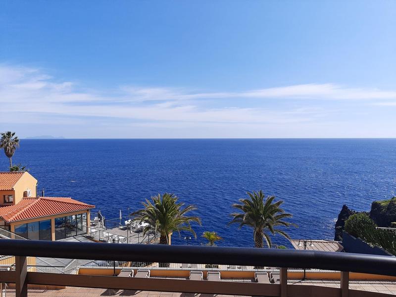 Widok z balkonu na niebieski ocean i palmy pod czystym niebem.