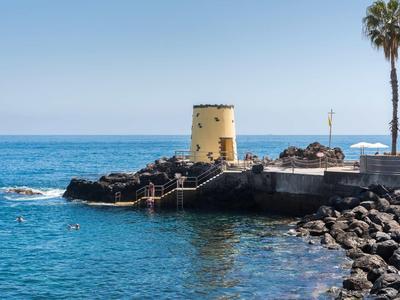 Ancienne tour jaune sur une côte rocheuse avec des palmiers et une mer bleue claire
