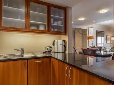 Coin cuisine moderne avec armoires en bois, réfrigérateur, bouilloire et coin repas en arrière-plan.