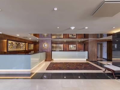 Réception d'hôtel moderne avec deux comptoirs, boiseries et tapis élégant.