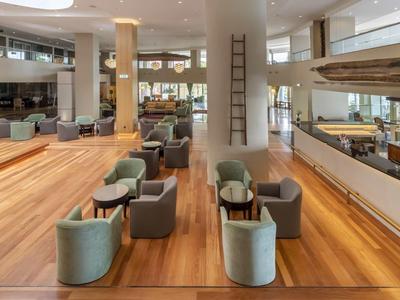 Espace lounge d'hôtel moderne avec sol en bois, zones de sièges et éclairage indirect.