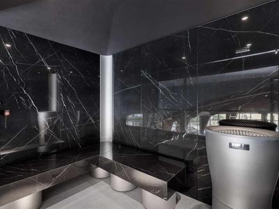 Sauna moderne avec murs en marbre noir, bancs argentés et poêle de sauna.