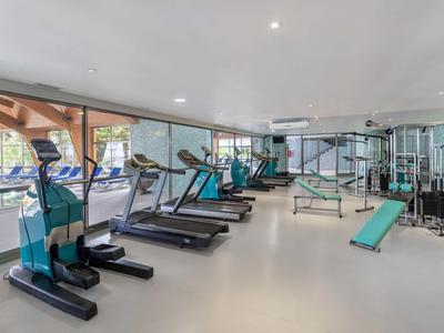 Lichte fitnessruimte met loopbanden, crosstrainers en krachtapparaten bij grote ramen.