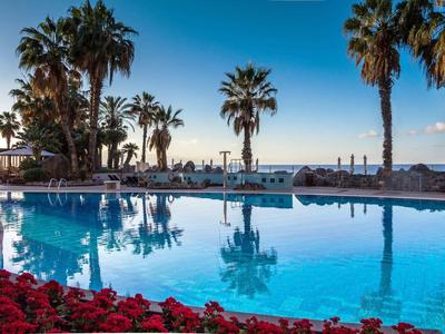 Piscine avec palmiers et chaises longues au bord de la mer au coucher du soleil.