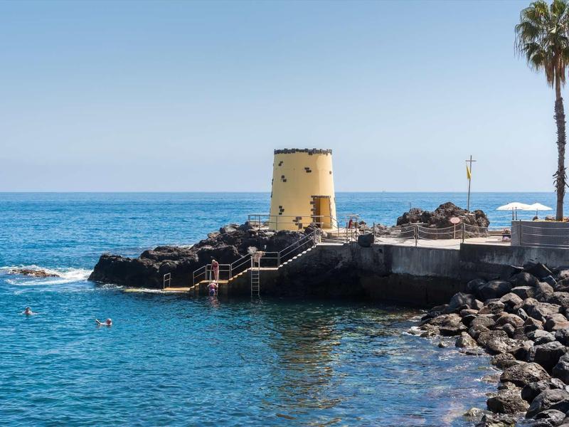 Ancienne tour jaune sur une côte rocheuse avec des palmiers et une mer bleue claire