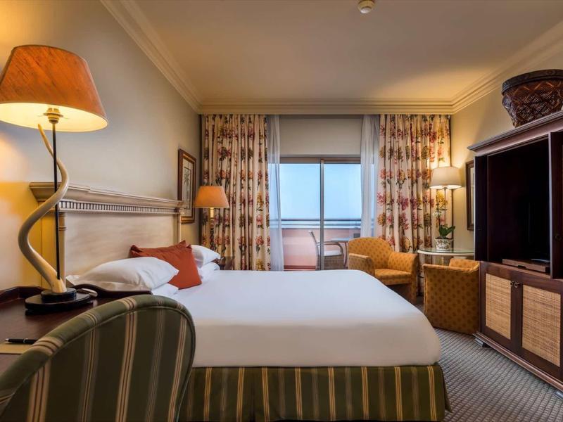 Chambre d'hôtel confortable avec lit double, fauteuils et balcon avec vue sur la mer.