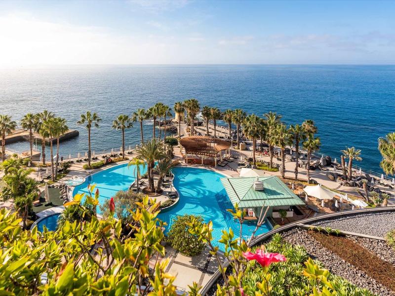Vue sur la piscine de l'hôtel et les palmiers avec l'océan en arrière-plan par temps ensoleillé.
