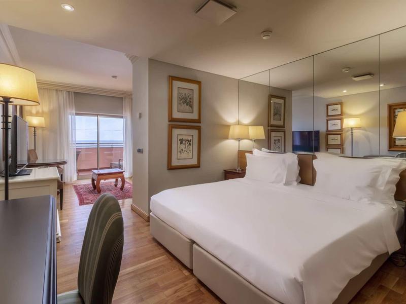 Chambre d'hôtel moderne avec lit double, bureau et vue sur un coin salon.