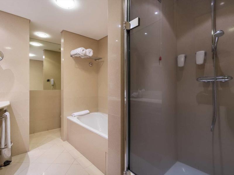 Salle de bain moderne avec douche, baignoire et serviettes dans un design beige clair.