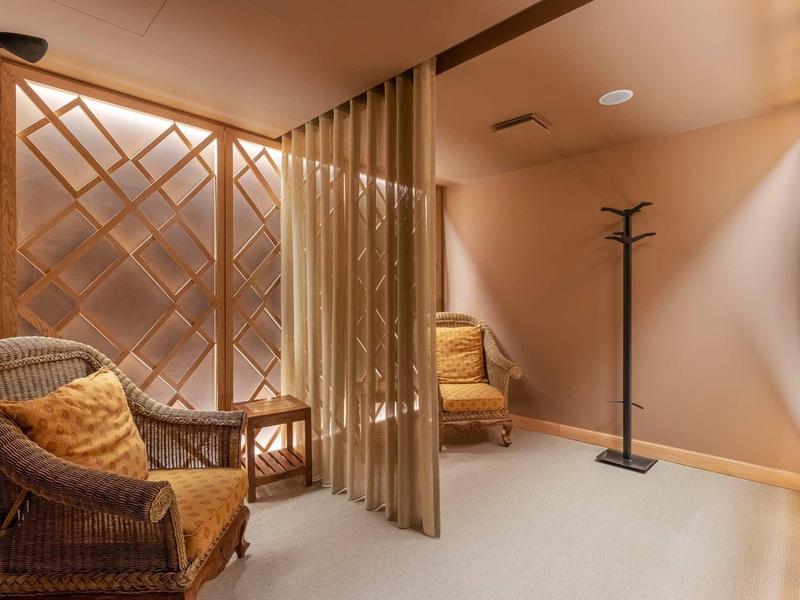 Espace confortable avec fauteuils en osier, table basse et cloison en lattes de bois dans un hôtel.