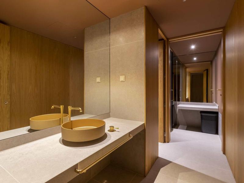 Salle de bain moderne avec lavabo rond, robinet doré et grand mur miroir.