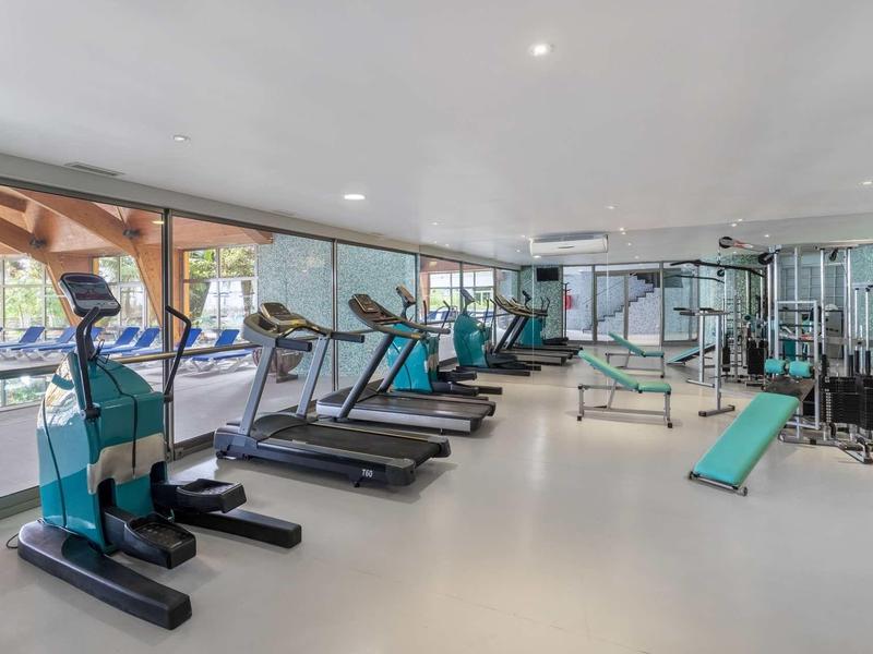 Salle de sport lumineuse et moderne avec tapis de course, stations de musculation et vue sur l'extérieur.