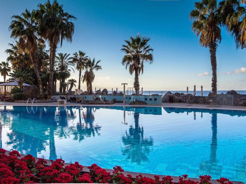 Piscine avec palmiers et chaises longues au bord de la mer au coucher du soleil.