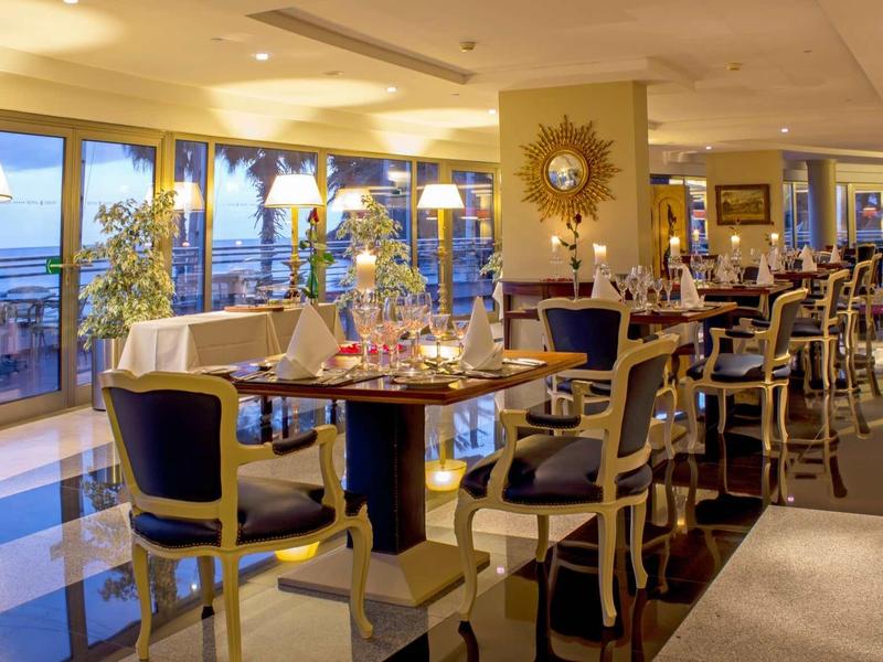 Intérieur de restaurant élégant avec tables dressées et vue sur la mer à travers de grandes fenêtres.