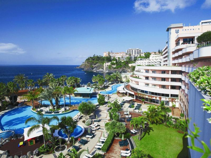 Hôtel de luxe avec piscines, palmiers et vue sur l'océan sur une côte ensoleillée.