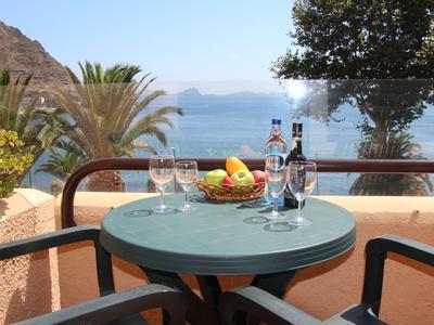 Kulatý stůl s košíkem ovoce, lahví vína a sklenicemi na terase s výhledem na moře.