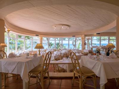 Elegantní restaurace s kulatými stoly, bílými ubrusy a velkými okny s výhledem na zeleň.