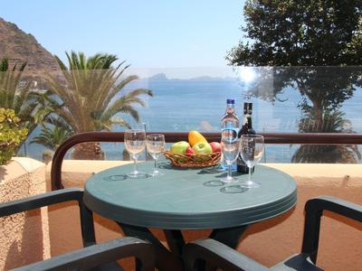 Runder Tisch mit Weingläsern und Obstschale auf Balkon mit Meerblick und Pflanzen.