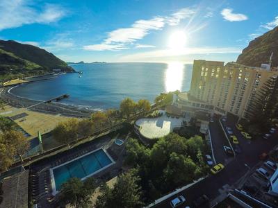 Vista de hotel con piscina, estacionamiento y playa a lo largo de la costa al atardecer.