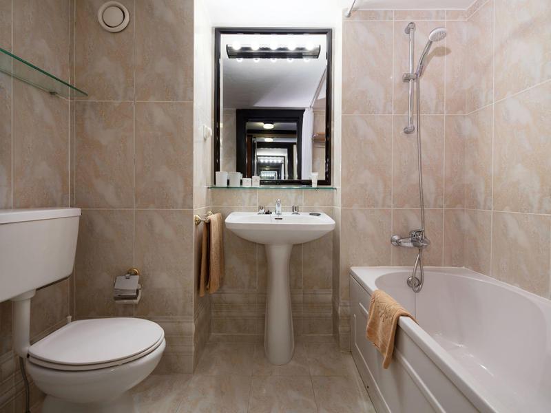 Malá koupelna s toaletou, umyvadlem, vanou a obklady ve stěnách v hotelu.