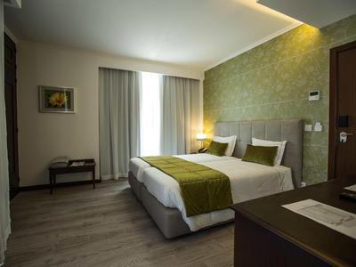 Modernes Hotelzimmer mit Doppelbett, grüner Wand und großem Fenster mit Vorhängen.