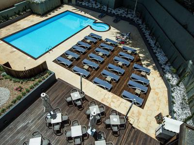 Blick auf einen Hotelpool mit Sonnenliegen und Tischen auf einer Terrasse.