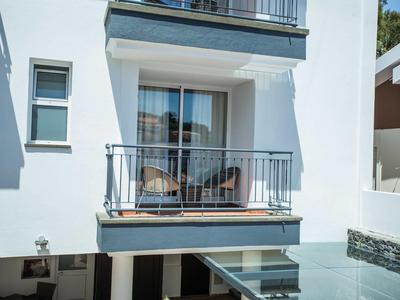 Balkon eines modernen weißen Gebäudes mit Stühlen und Glasgeländer im Urlaub.